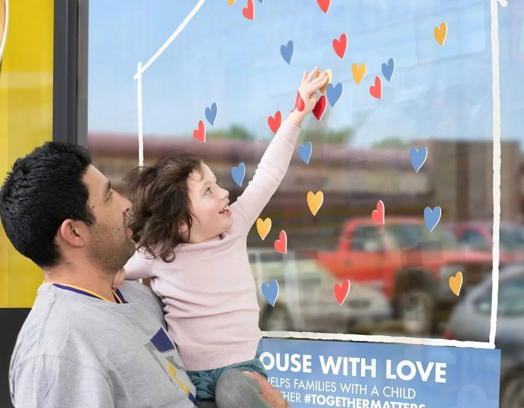 Dad carrying a smiling child. Child points at McDonald signage
